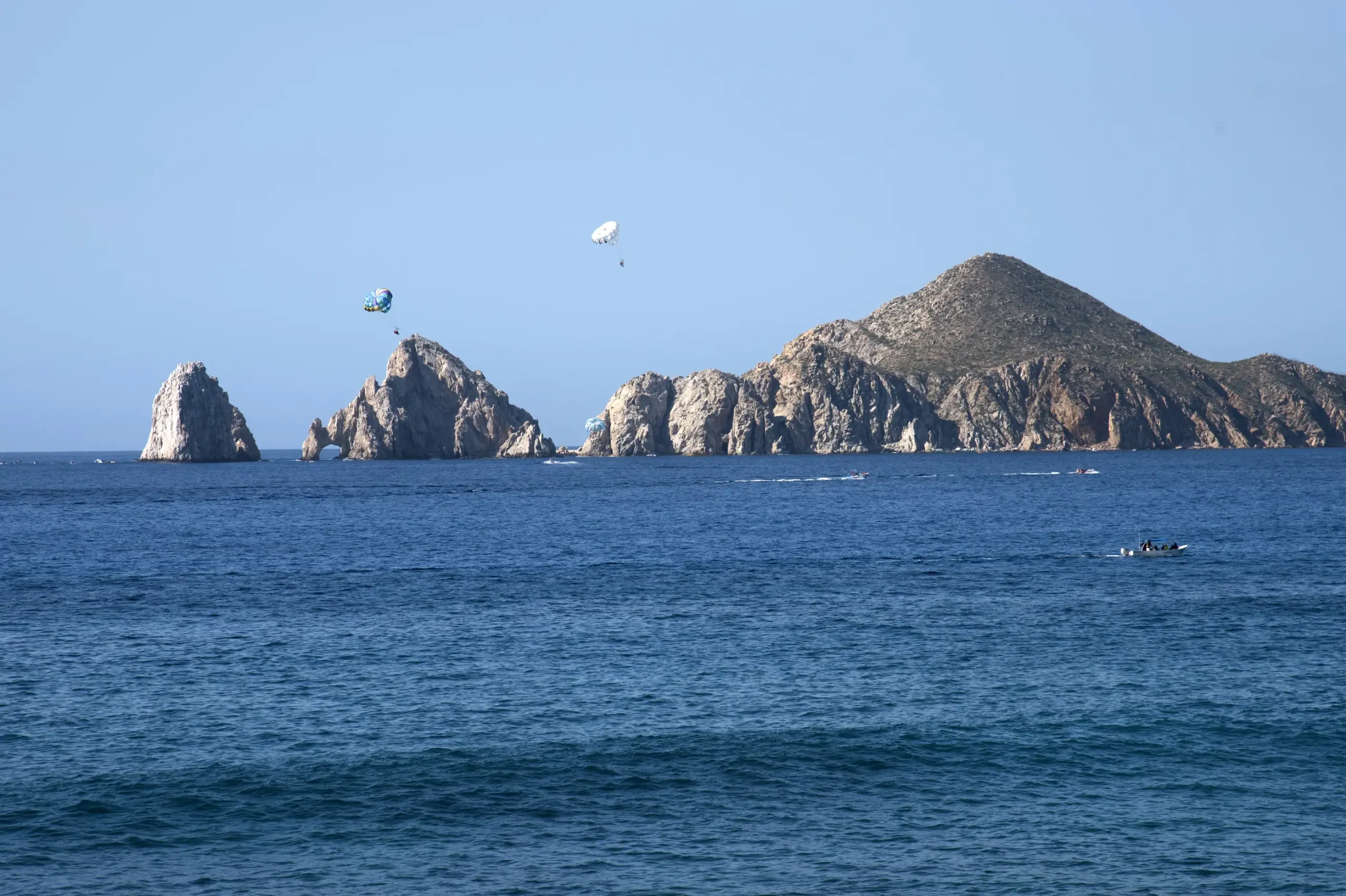 Boats and parasails near the rocky coastline at Land's End in Cabo San Lucas.