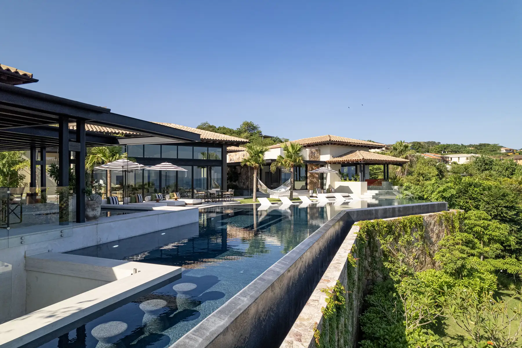 Villa terrace with an infinity pool, shaded seating and surrounding greenery.