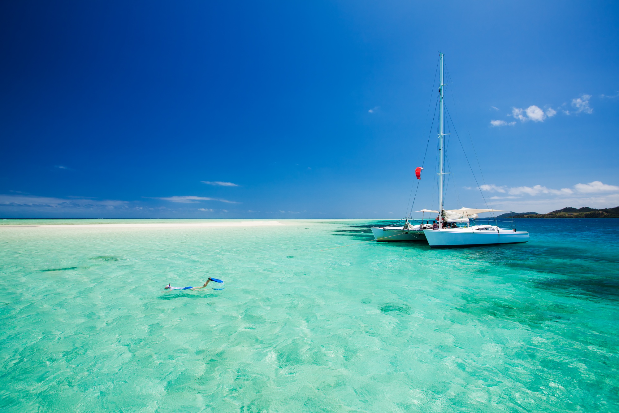 Snorkelers in shallow, clear water beside a charter catamaran at anchor