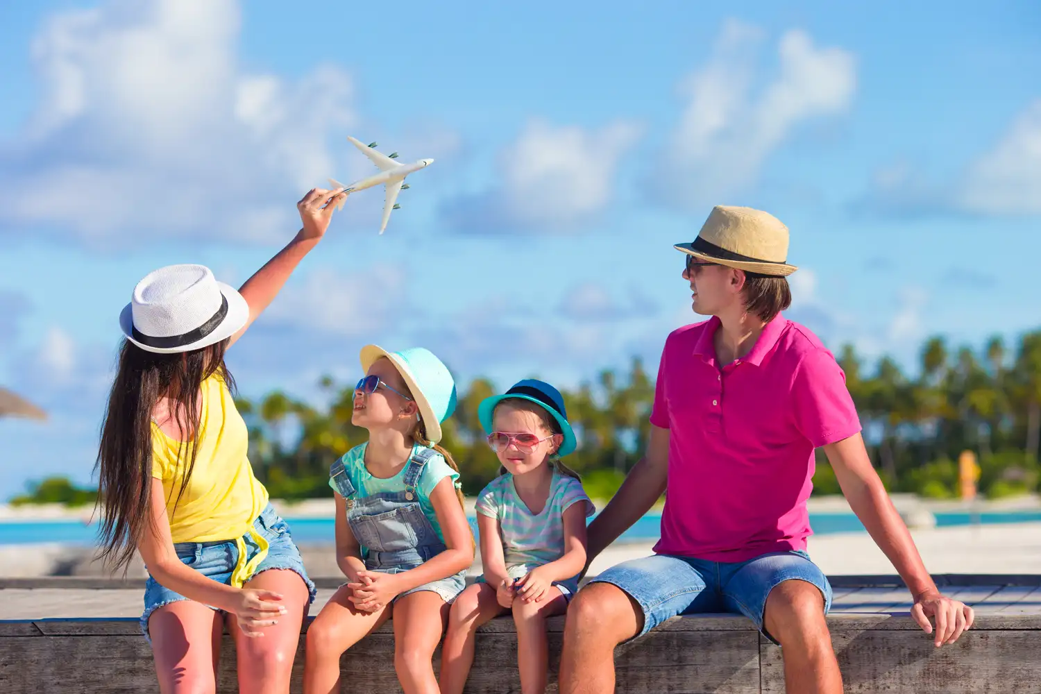Two adults and two children sitting beside the water with a toy airplane.