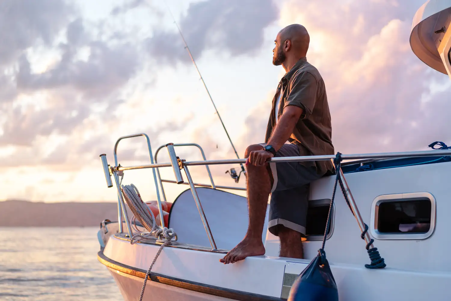 A man sitting aboard a boat with a fishing rod at sunset.