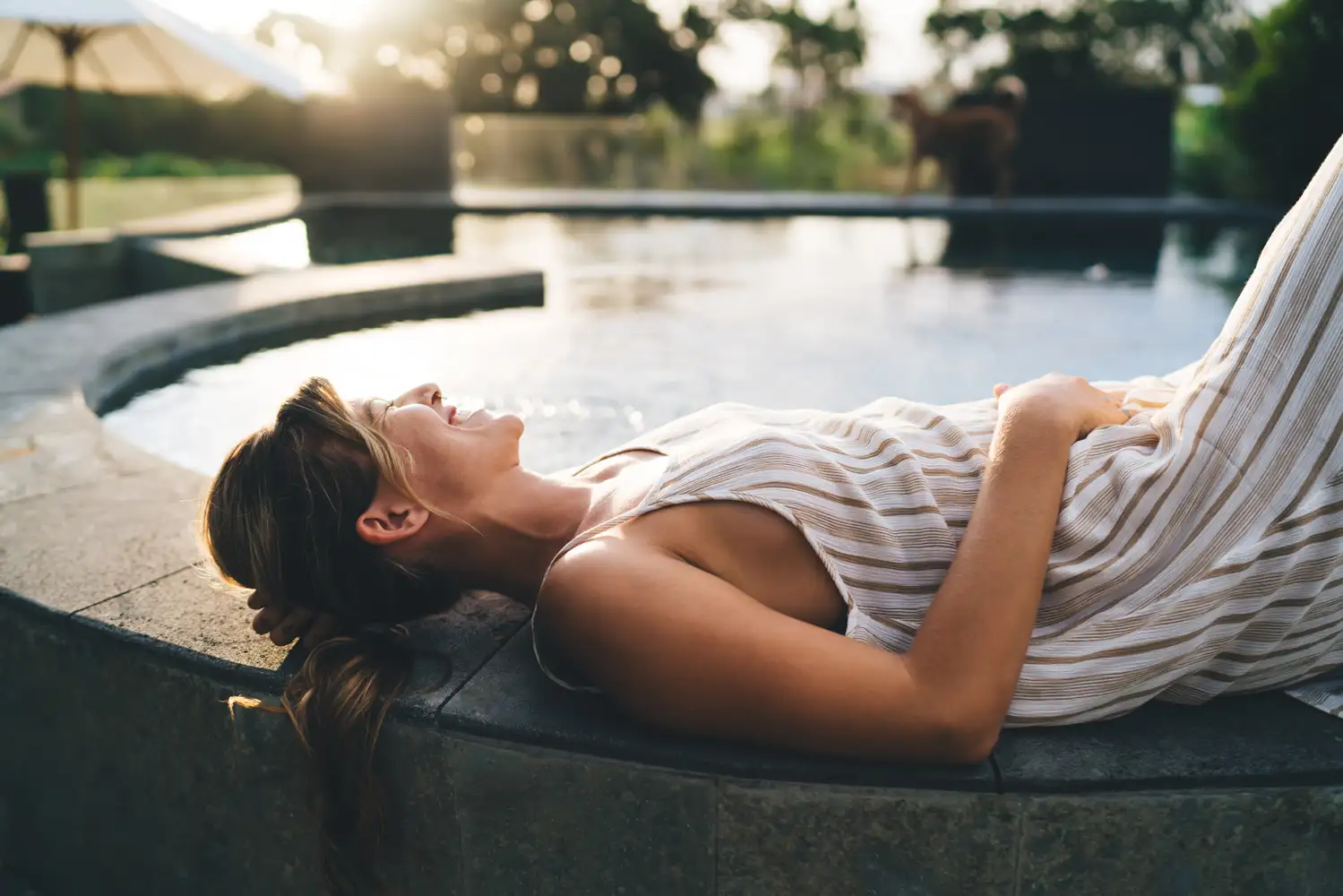 A woman resting beside a swimming pool in warm evening light.