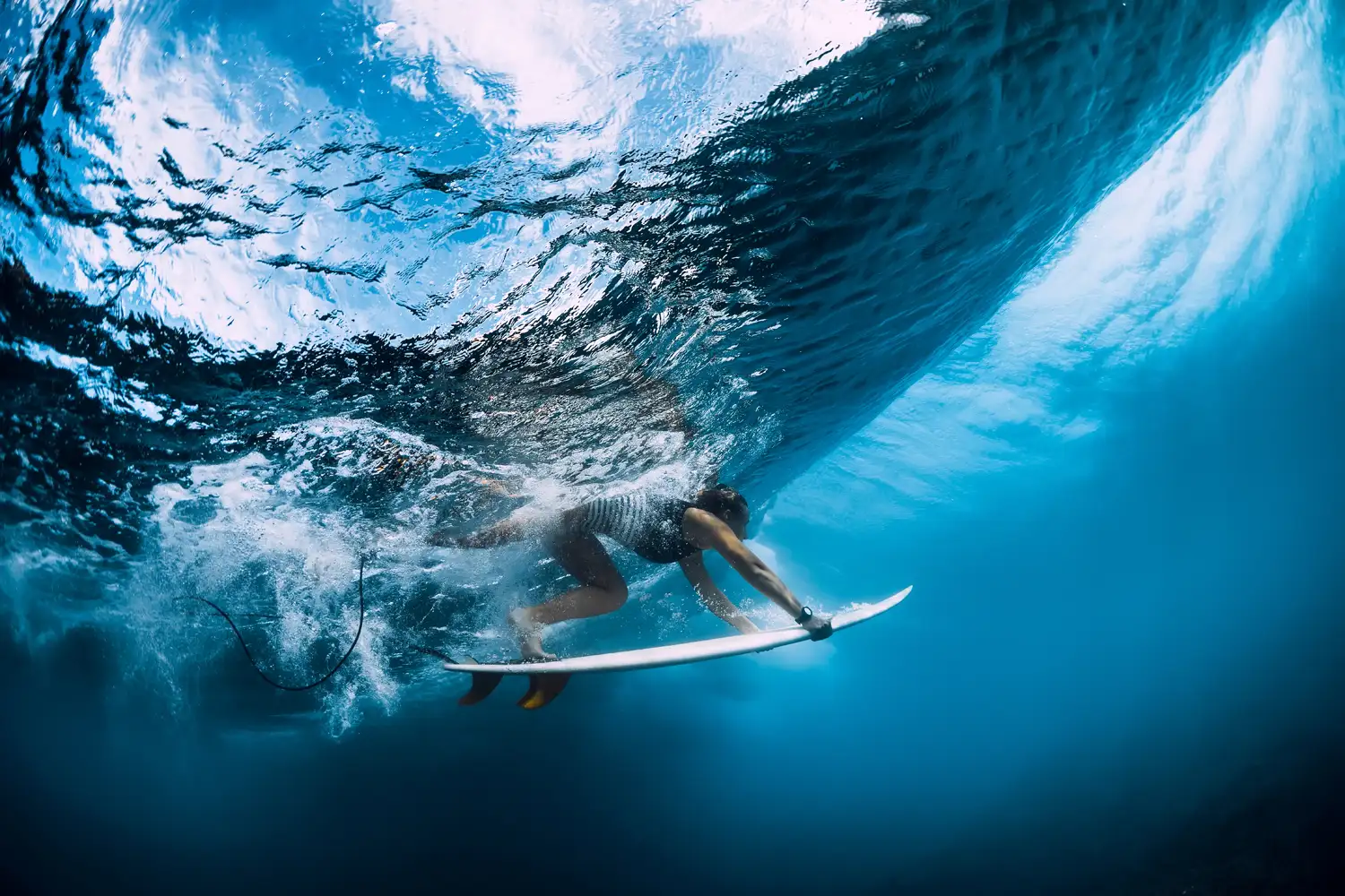 Underwater view of a surfer duck-diving beneath a breaking wave.
