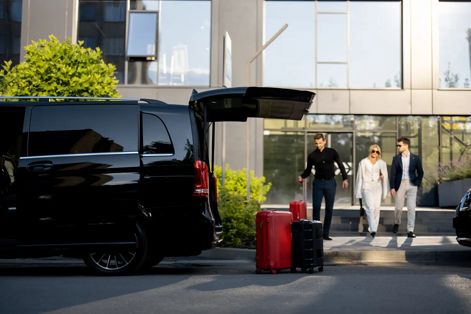 Travelers with suitcases beside a black passenger van.