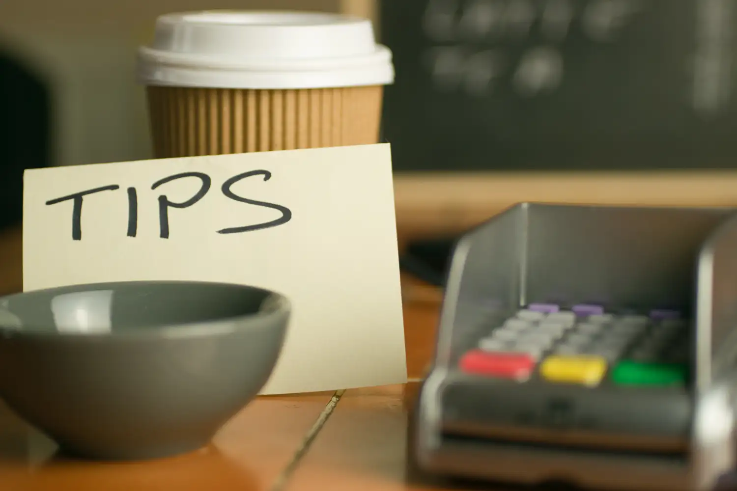 A handwritten tips sign beside a bowl, coffee cup and payment terminal.