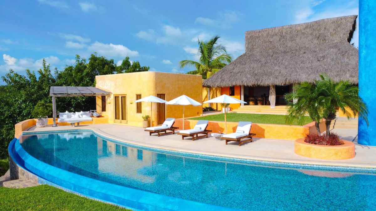 The ochre walls, palapa roof and curved pool of Casa Torre del Cielo, a rental villa in Costa Careyes